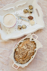 Fototapeta na wymiar Whole wheat bread with sesame seeds and flax seeds in baking form. Fresh quail eggs, seeds and flour on a wooden tray