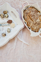 Fototapeta premium Whole wheat bread with sesame seeds and flax seeds in baking form. Fresh quail eggs, seeds and flour on a wooden tray
