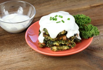 Pile of homemade kale pancakes with dressing.  Fried vegetable pancakes on the plate, brown table, ...