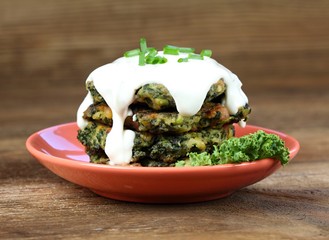 Pile of homemade kale pancakes with dressing.  Fried vegetable pancakes on the plate, brown table, ...