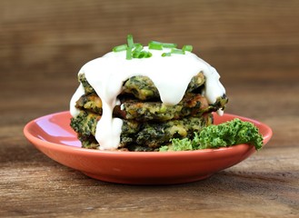 Pile of homemade kale pancakes with dressing.  Fried vegetable pancakes on the plate, brown table,  decorated with fresh kale.