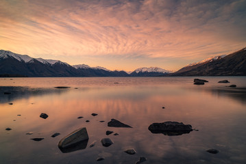 Scenic view of a beautiful blue lake with snow capped mountains in the background and a colorful sunset sky in New Zealand South Island.