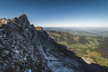 agged rock formations on Mount Pilatus overlooking a valley in the Swiss Alps with snowy mountain peaks in the background in Lucerne, Switzerland