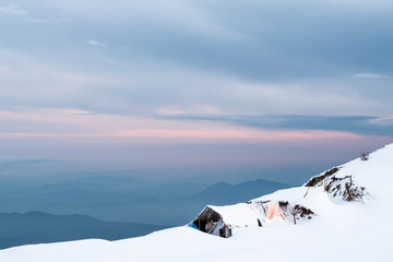 snowy landscape of high mountains with small shed covered by white snow at sunset in the Himalayas