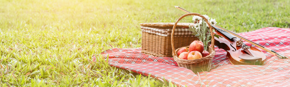 Picnic Basket Fruit Bakery And Violin On Red Cloth In Garden, Copy Space, Banner Size.