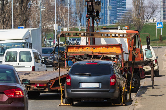Loading a broken passenger car onto a yellow tow truck in the middle of a busy street on a sunny day. The central part of the big city.