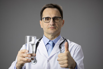 Nutritionist in white coat with a stethoscope on his neck holds a glass of water in his hands and points a finger at it. Healthy lifestyle. Thirst. Proper nutrition. Water-salt balance. Thumb up. Like