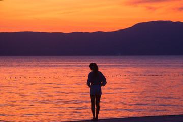 silhouette of a girl sitting on a pier at sunset of the sea