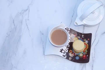 Fancy decorative cup and saucer set with space for a buscuit on the side. And a white tea pot on a white marble background