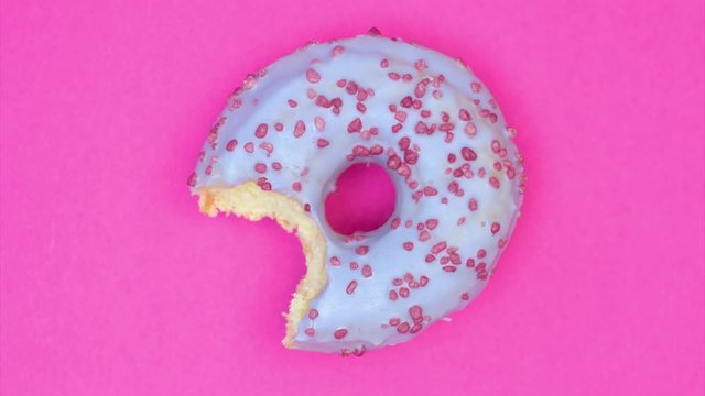 Animation with blue glazed donut on pink background. Disappearing bite by bite. Copy space