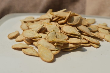 Many pumpkin seeds are gathered together on a white container.