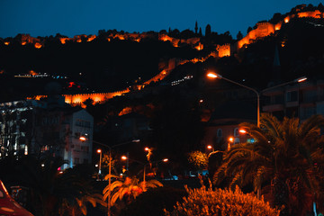 Night view image of old city near sea with ancient castle, houses and stone walls scenery between lights from Alanya Antalya Turkey