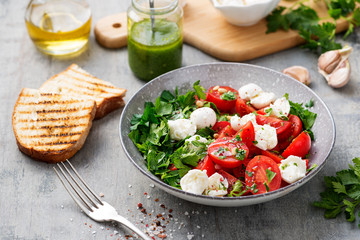 Fresh classic caprese salad with cherry tomatoes, mozzarella balls,parsley leaves and pesto sauce. isolated on white background