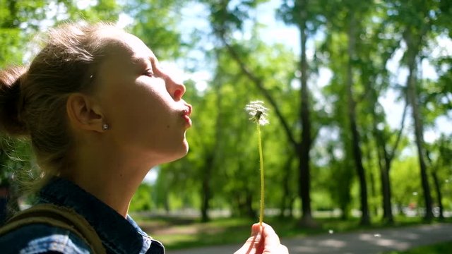 Woman blowing on white dandelion in summer park