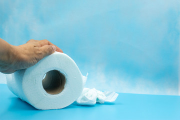 Hand is holding toilet tissue paper on blue background. Toilet paper (sometimes called toilet roll or loo roll in Britain) is a tissue paper product.