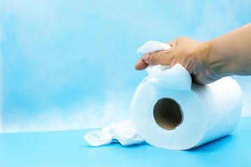 Hand is holding toilet tissue paper on blue background. Toilet paper (sometimes called toilet roll or loo roll in Britain) is a tissue paper product.