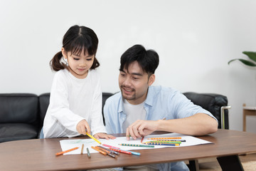 A pair of young Asian father and daughter are drawing in the living room