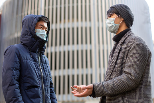 Two asian young men in facial medical masks against covid-2019 talking to each other. Outside. Virus protection. Chinese coronavirus outbreak concept. Pandemic disease.