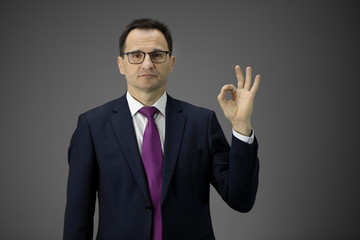 Pleasant looking male middle aged business owner in formal clothes, tie shows ok sign on isolated grey background with copy space. Handsome man, business success, leadership, achieving goals, concept