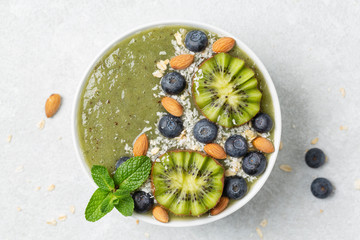 Breakfast green smoothie bowl topped with kiwi, blueberry, almond and coconut flakes on light grey background. 