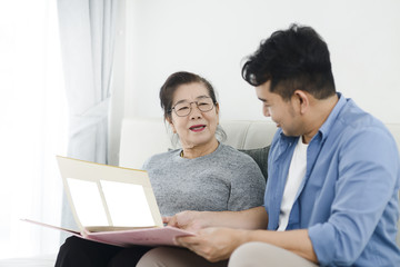 Asian man and his mother looking at photo album together while staying at home.