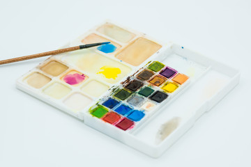 Palette of watercolors on white background. Brush mixing colors, blue, yellow and magenta in the palette.