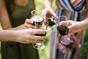 Celebration. People holding glasses of red wine making a toast outdoor on green background