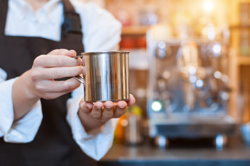 Closeup female hands are holding metal cup of aromatic coffee. Barista woman  prepared, brewed espresso, americano, latte cappuccino using professional machine in cafe, restaurant. Take away, to go.