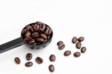 Roasted coffee beans in a coffee spoon on a white background.
