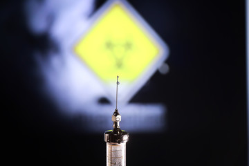 Medical syringe with a needle and a cure for the virus. A drop of drug flows down the needle....