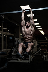 Fototapeta na wymiar abdominal muscles training of young bearded caucasian man on horizontal bar in dark sport gym