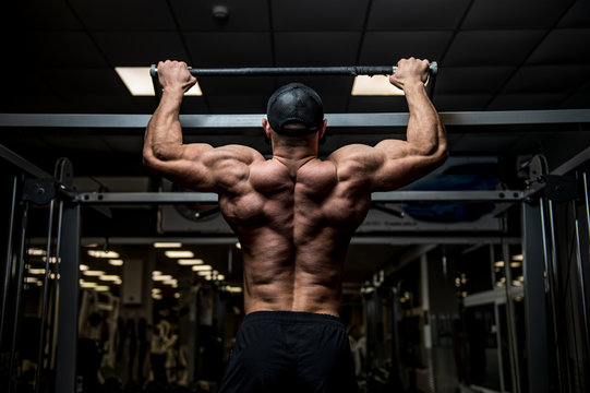 strong young man lifting his heavy weight body during chin ups on horizontal bar in sport gym during workout training