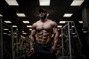 Fototapeta na wymiar handsome young strong bearded caucasian male in dark sport empty gym with fitness equipment indoors