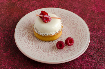 Contemporary coconut mini mousse tart decorated with fresh raspberries on white plate on red background