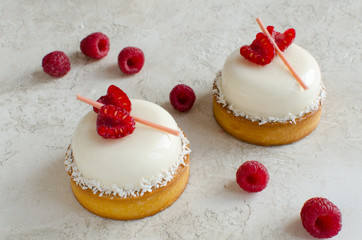 Contemporary coconut mini mousse tarts decorated with fresh raspberries on light background