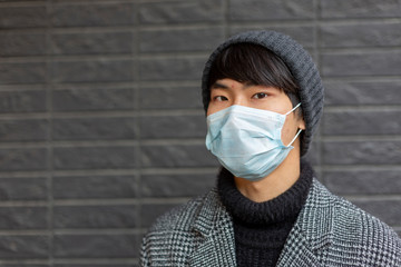 Portrait of asian young man . Chinese guy in medical protective mask against covid-2019 . Outside. Grey background. Pandemic disease. Virus protection. Chinese coronavirus outbreak.