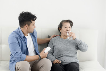 Asian man giving medicine to his mother, stay home and COVID-19 concept.