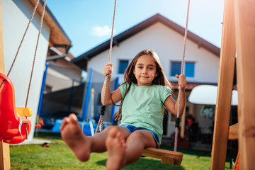 Fototapeta na wymiar Portrait of a little girl sitting on the swing at backyard