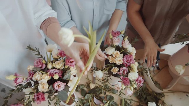 Top view close-up shot of hands of female and male florists arranging flower bouquets in hatboxes while working in team at table in workshop