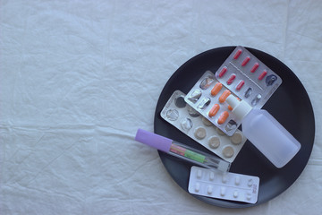 
A black metal plate with a thermometer, antipyretic and antiviral drugs on a white disposable diaper. Anti - COVID Flat Lay
