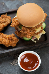 Burger with fried chicken strips on a wooden serving board, vertical shot, elevated view