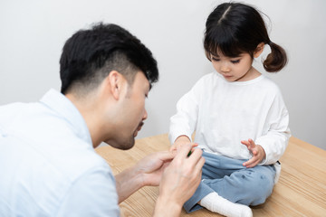 A pair of young Asian father and daughter are applying nail polish in the living room