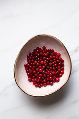 lingonberry berries in white bowl on marble table