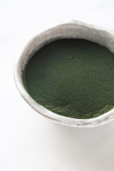 Organic spirulina powder in rustic bowl on white marble background