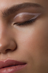 Fototapeta premium Close up half portrait of a face with beautiful skin and nude makeup, eyeliner and long eyelashes, puffy natural lips and white flowers. Fashion photography. Cosmetology and spa. Freshness of spring