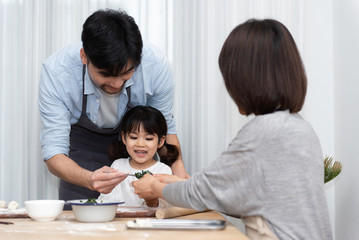 Young Asian mom and dad making dumplings with daughter