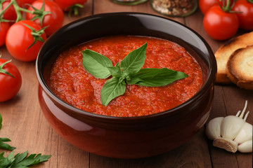 Spicy Homemade Gazpacho Soup with basil. Ready to Eat. Ingredients around the bowl of gazpacho tomato soup. Tomatoes cherry, salt, pepper, garlic, bread croutons and parsley. Basil decorates the dish