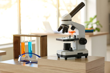 Microscope with test tubes and protective glasses on table in classroom