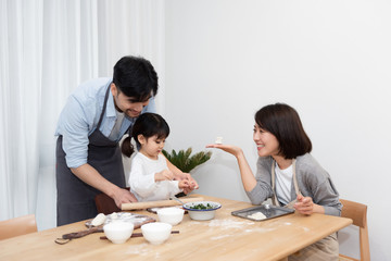 Young Asian mom and dad making dumplings with daughter