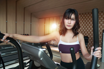 Fototapeta premium Happy and smiling young beautiful asian woman in sportswear jogging or working on exercise machine in gym. Cute and sporty girl running in fitness. (sport concept)
